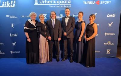 Ukin urheilugaalassa juhlivat kuusi ihmistä, jotka poseeraavat urheilugaalan taustakuvassa